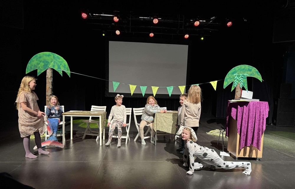 Teaterelever i forestilling omgitt av palmer  - Klikk for stort bilde